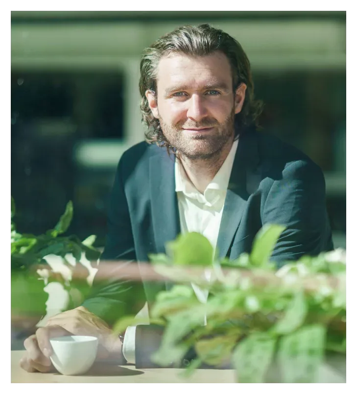 Rob Segers Bitcoin advisor in suit behind window with cup of coffee