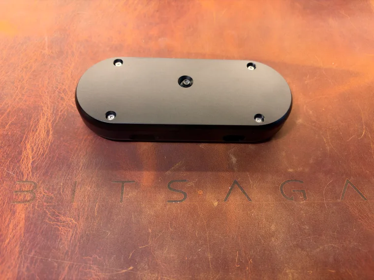 The black SeedSigner+ Premium from behind at a low angle, showing the four-screw back plate, the camera lens and both port cutouts along its bottom edge