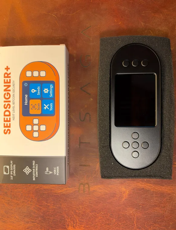 What arrives: the orange printed SeedSigner+ box standing beside the device itself, seated in a black foam tray