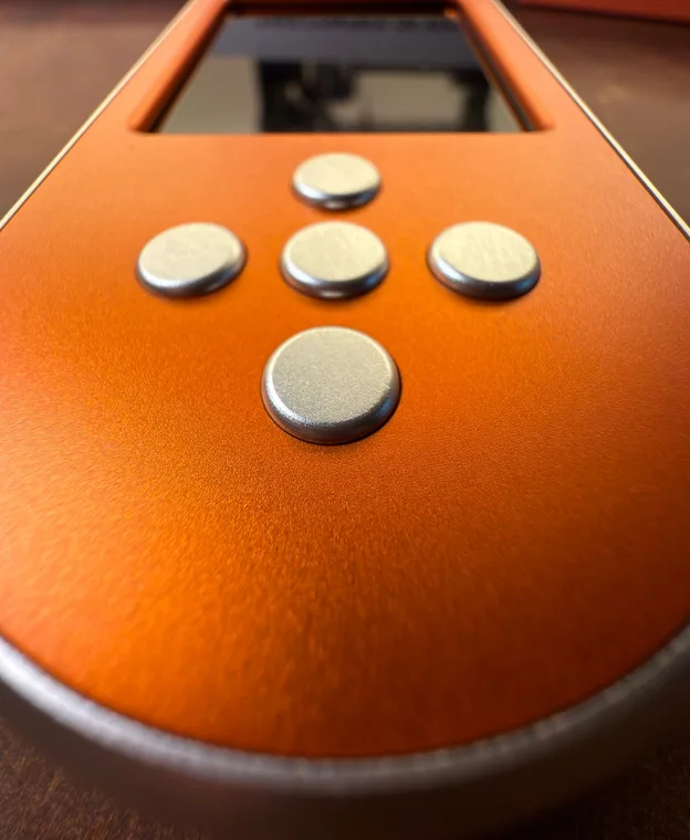 Close-up of the orange SeedSigner+ Premium's controls, silver buttons against the anodised orange case, with the camera opening in the top edge