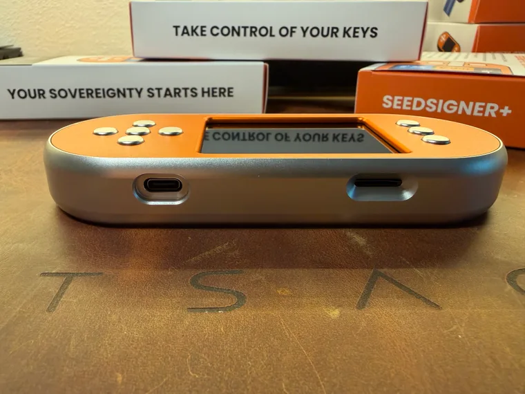 The bottom edge of the orange and silver SeedSigner+ Premium, with the USB-C power port on the left and the microSD slot on the right