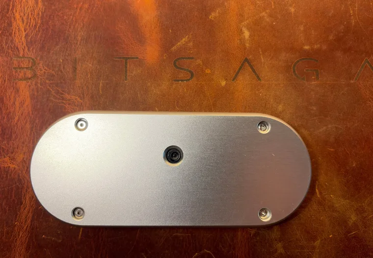 The back of the silver SeedSigner+ Premium, a bare brushed aluminium plate held by four corner screws with the camera lens in the middle